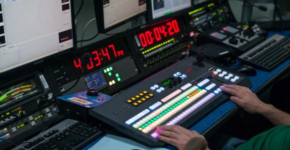 Producer using control room equipment: timer, soundboard, screens