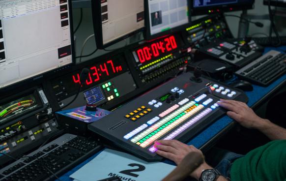 Producer using control room equipment: timer, soundboard, screens
